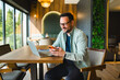 © djile - Smiling man using smartphone while working on laptop in cafe
