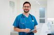 © InsideCreativeHouse - Portrait of young male surgeon standing with clipboard in hospital corridor, professional healthcare worker in modern clinic interior, medicine, patient care and medical service concept