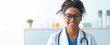 © Prostock-studio - A woman doctor stands in a modern office with a friendly smile. She wears glasses and a white coat, showing professionalism. The background is bright and simple, indicating a healthcare setting.