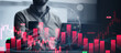© Prostock-studio - A person is engaged in digital trading, holding a smartphone in one hand while examining market data. Charts display buy and sell signals with various price movements and patterns.