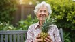 © Alex Pios - Elderly woman sitting on a garden bench and holding a pineapple in her lap while smiling