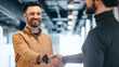 © Prostock-studio - Two men stand in a well-lit office space, engaging in a handshake. They are smiling and appear to be having a positive interaction. The environment shows modern design elements and bright lighting.