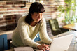 © Davor - Woman working on laptop in cozy home kitchen