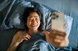 © Davor - Smiling woman in bed video calling at home