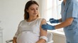 © olga_demina - A pregnant woman sits in a clinic chair as a healthcare professional administers a flu vaccination, promoting health and prevention during pregnancy.