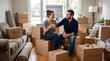© NORN - A happy young couple taking a break from packing and moving into their new home. They are sitting on cardboard boxes in the living room