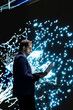© DC Studio - Technician monitors deep learning AI model patterns using laptop. RD lab employee studies artificial intelligence neural network algorithm nodes on digital wall to understand processing using notebook