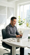 © Alena Yakusheva - Mature man in a grey shirt working on a laptop at a white desk in a bright contemporary office, focused professional, remote work lifestyle.