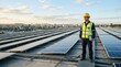 © hobonski - Solar power engineer in a yellow hard hat and safety vest standing on a roof covered with solar panels during a clear sunset.