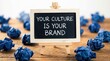 © Wajahat - Small chalkboard on a wooden easel with 'your culture is your brand' surrounded by crumpled blue paper on a wooden desk