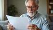 © miss irine - Elderly man with glasses reads paper document at home. Concentrated on information, looking at text, thinking deeply. Mature person reviewing notes, planning future. Senior male studies material.