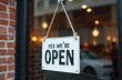 © miss irine - White sign with black text reads YES WERE OPEN. It hangs on a glass door with brick wall outside. Blurred background shows warm lights and car.