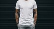 © Velvet - Man with full sleeves of intricate tattoos wearing a white t-shirt and grey pants standing against a dark wall