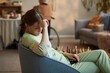 © DragonImages - Middle aged Caucasian female caregiver sitting with head in hand in nursing home, expressing stress and burnout during elder care