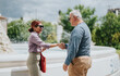 © qunica.com - Two colleagues exchange a friendly business handshake and smile beside a public fountain. A casual outdoor meeting shows a professional greeting between two people.