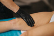 © qunica.com - Therapist wearing black gloves performs a leg massage on a client at a beauty center. Close-up shows a gloved hand applying treatment to the upper thigh on a treatment table.