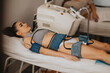 © qunica.com - Young woman receives noninvasive body contouring treatment with electrode pads on abdomen, thighs and arms.