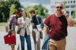 © qunica.com - A middle aged businessman walks outdoors talking on his mobile phone while holding a jacket. Colleagues stand behind him consulting a tablet and papers, suggesting a casual work meeting on campus.