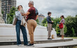 © qunica.com - Business colleagues hold an outdoor discussion by a city fountain. Two pairs of adults exchange documents and talk in a park setting.