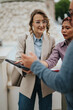 © qunica.com - A group of business colleagues reviews documents together while standing near a fountain. Casual outdoor meeting with coworkers discussing notes and a tablet in a public plaza.