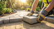 © ViskBx - Closeup of a construction worker installing concrete pavers on a sand base to create a garden pathway in a sunny backyard setting
