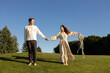 © Anna - beautiful, happy, barefoot newlywed couple stands on grass holding hands under cloudless sky on sunny day. woman in dress holds flower wreath. A loving couple, a moment of unity, a bride and groom