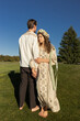 © Anna - barefoot newlywed couple stands on grass holding each other's arms under cloudless sky on a sunny day. A woman in an embroidered dress holds a man close. A tender moment of unity, the bride and groom