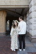 © Anna - Beautiful, elegant, and happy newlyweds next to each other, looking in the same direction. A loving couple, a wedding. A young woman, the bride, in a simple embroidered dress and a wreath