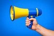 © Pro Clipart - Close up view of a male hand holding a bright yellow and blue megaphone against a solid vivid blue background. This striking photo is highly suitable for public announcements and marketing.