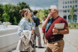 © qunica.com - A man and a woman business colleagues talk outdoors while holding a tablet and jacket. They stand in a city plaza engaged in a casual professional conversation.