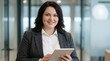© StocksJust4You - Smiling Caucasian young professional businesswoman, corporate marketing manager holding digital tablet, standing in modern office, confident pose, fintech concept