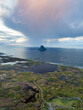 © AmazingAerialAgency - Aerial view of the rugged coastline of Andoya featuring the iconic conical Bleiksoya island under dramatic rain clouds and a soft sunset glow in Andoy, Nordland, Norway.