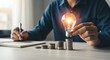 © Pixel Stone - Businessman holding a glowing light bulb over stacked coins on a desk with a notebook