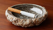 © Yuliia Yevdokymova - Close-up of lit cigarette with burning ash resting on edge of textured stone ashtray on polished wooden table