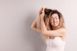 © New Africa - Unhappy woman trying to brush her tangled hair on light grey background, space for text