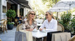 © Sachin - Two happy mature women laughing at an outdoor cafe with coffee and shopping bags on a sunny day