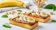 © Kamrul - Delicious banana toast with peanut butter and nuts on white background
