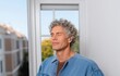 © Road Red Runner - Middle-aged man with a hearing aid in his ear closes his eyes, focusing on the sounds of birds outside a clinic window