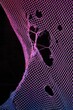 © Kalivmasa - Vibrant pink and blue netting with holes against a dark background