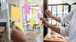 © Talia - Creative professionals actively brainstorming and organizing ideas using colorful sticky notes on a clear glass board.