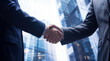 © Talia - Two businessmen in suits shaking hands, symbolizing agreement with blurred corporate building.