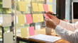 © Talia - Person's hands organizing ideas on a glass board with colorful sticky notes in a modern office.