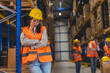 © Dragana Gordic - Tired Female Warehouse Worker in Hard Hat and High-Visibility Vest Leaning on Racking in Logistics Warehouse