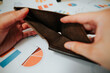 © Sergio - A person uses hands to hold an empty wallet, showing a lack of cash. The background features various financial documents and charts related to budgeting and expenses
