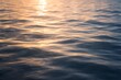 © muhagraph - Close-up of rippling water reflecting the warm glow of the setting sun, creating a serene and tranquil natural scene with gentle waves and shimmering light.