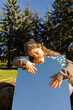 © Anna - Beautiful young woman or adult teenager hugging large mirror in park on sunny day. Reflection of face, hands and sky. Dreams, relaxation. Atmospheric photo. Love life, well-being. Spring walk outdoors