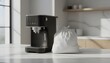 © antuanetto - White plastic trash bag stands beside a modern black espresso coffee machine on a marble countertop in a bright kitchen for a waste management and cleaning concept
