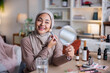 © Jovo Jovanovic/Stocksy - Woman in hijab applying makeup with brush and mirror.