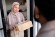 © Jovo Jovanovic/Stocksy - Woman wearing a hijab receiving a package at her front door