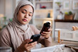 © Jovo Jovanovic/Stocksy - Woman in hijab checks product information on her phone.